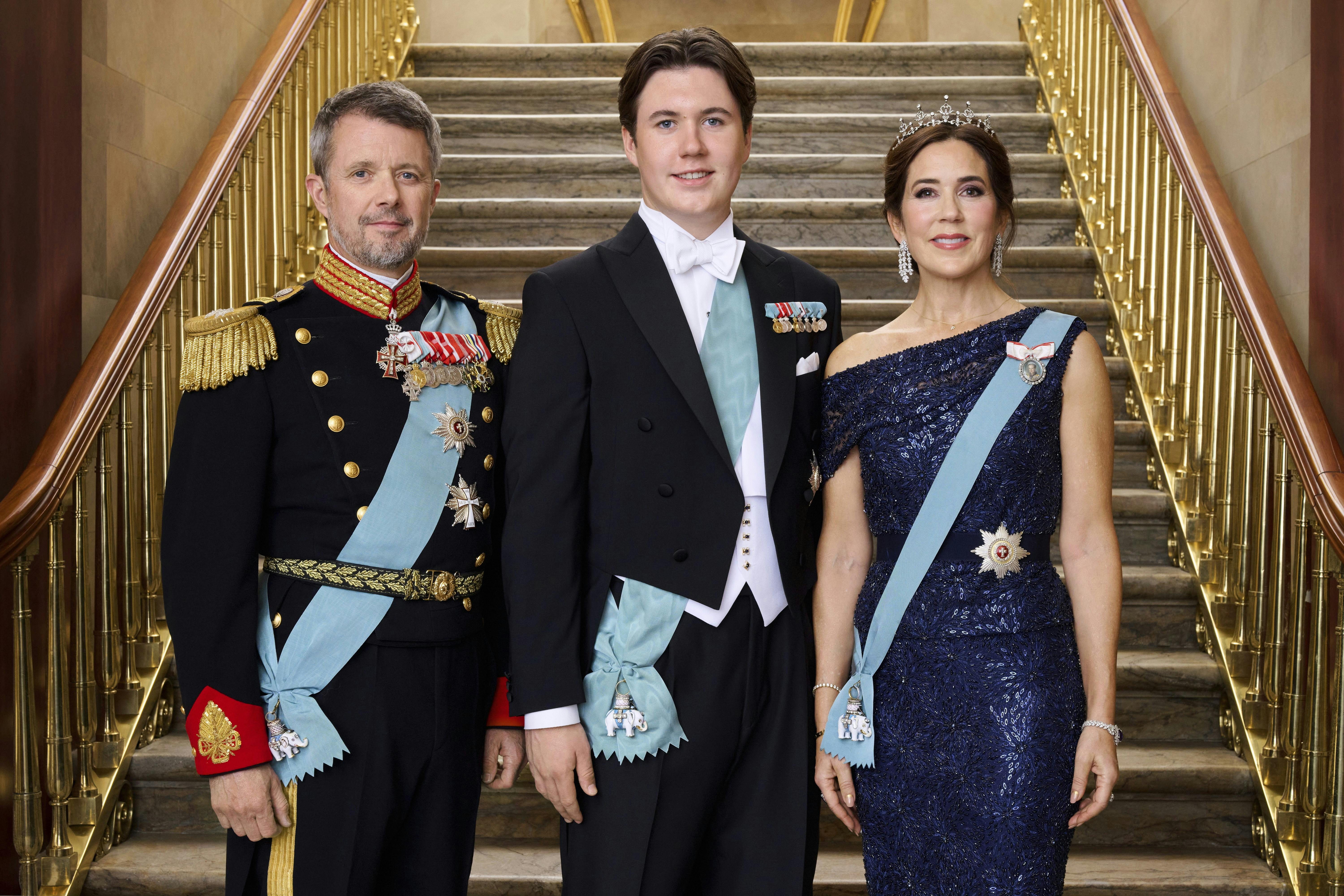 Prins Christian i gallatøj sammen med kronprins Frederik og kronprinsesse Mary foran en trappe.