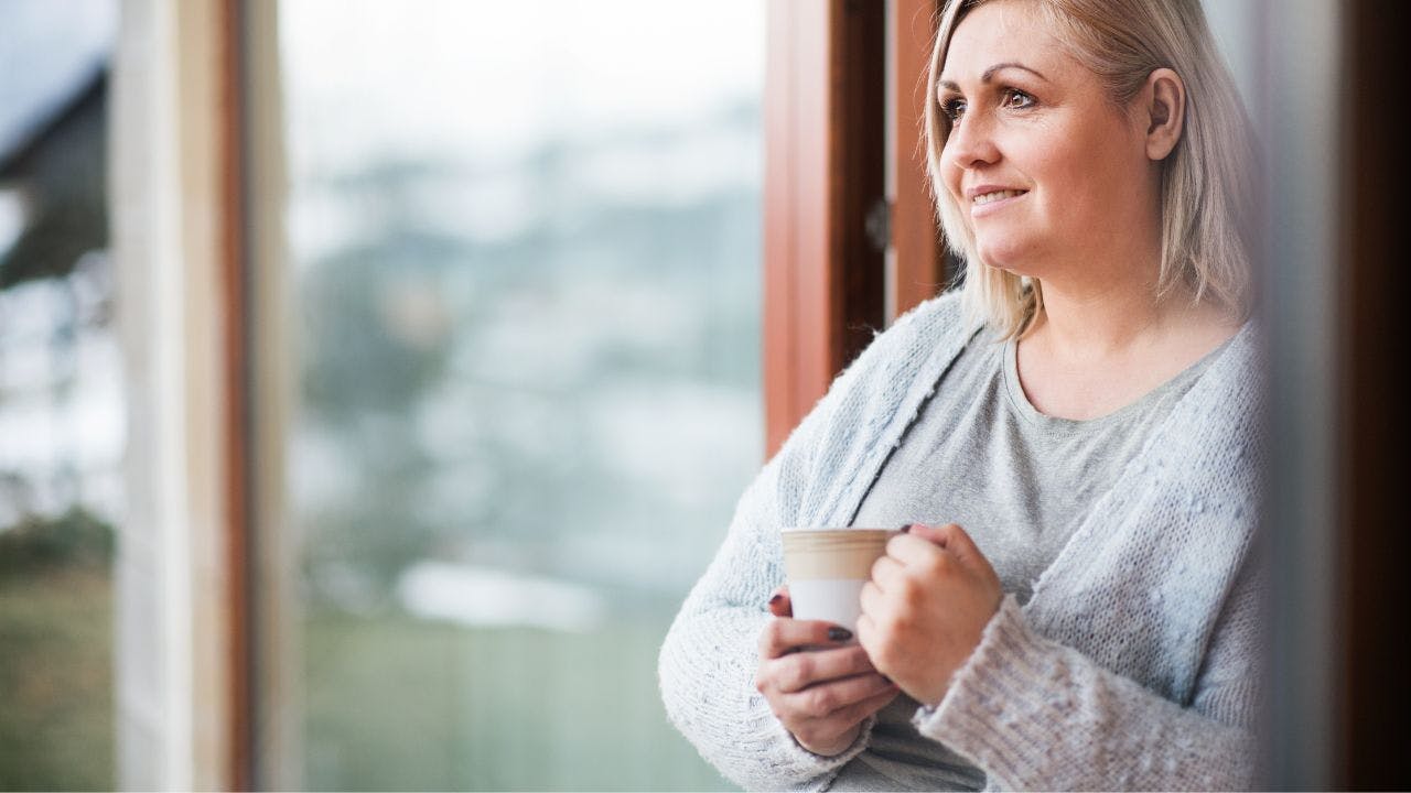 Kvinde står i dørkarm med kaffekop i hånden og kigger udenfor