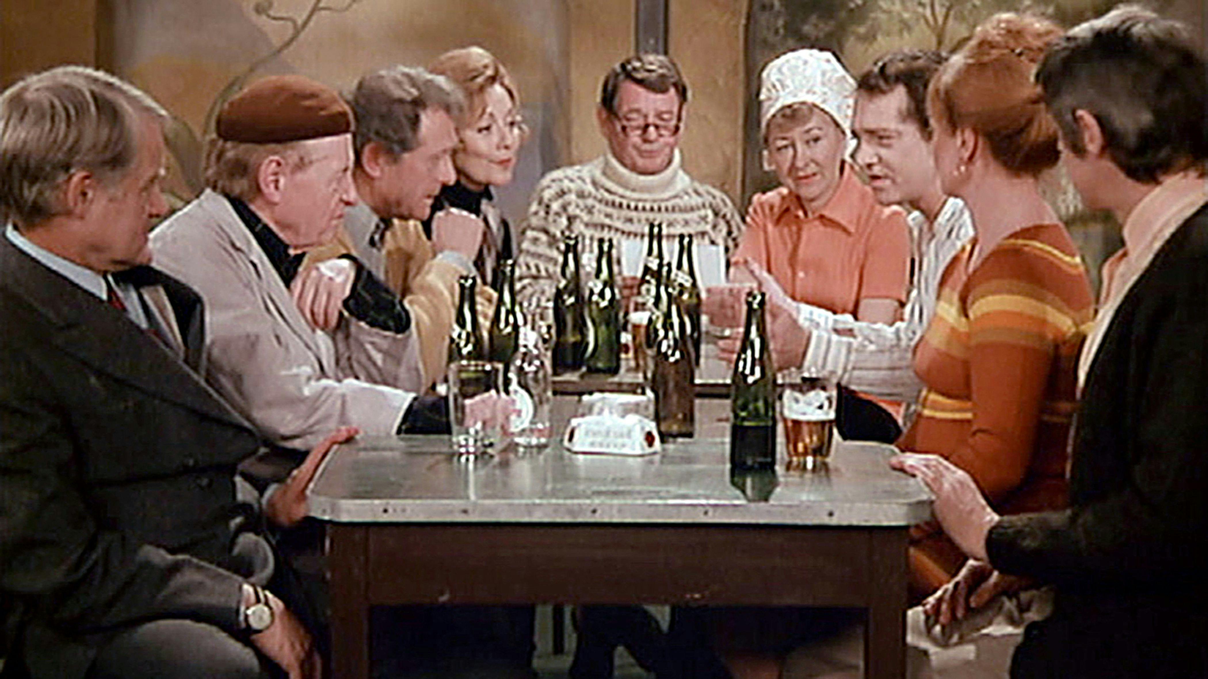 En gruppe af mennesker, der sidder omkring et bord og taler og drikker øl.