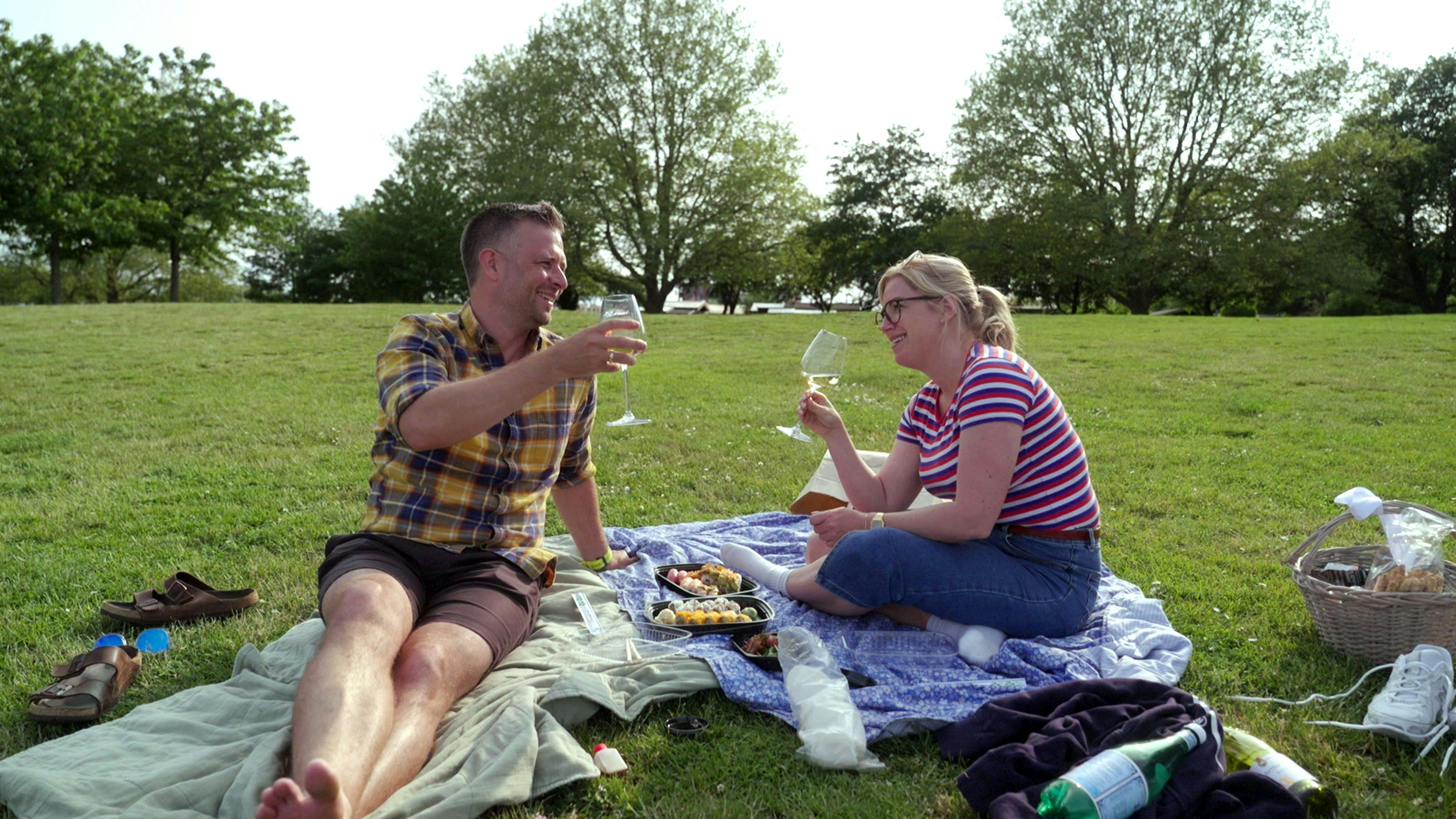 Et midaldrende par, der sidder på et picnictæppe i en park og skåler i hvidvin.