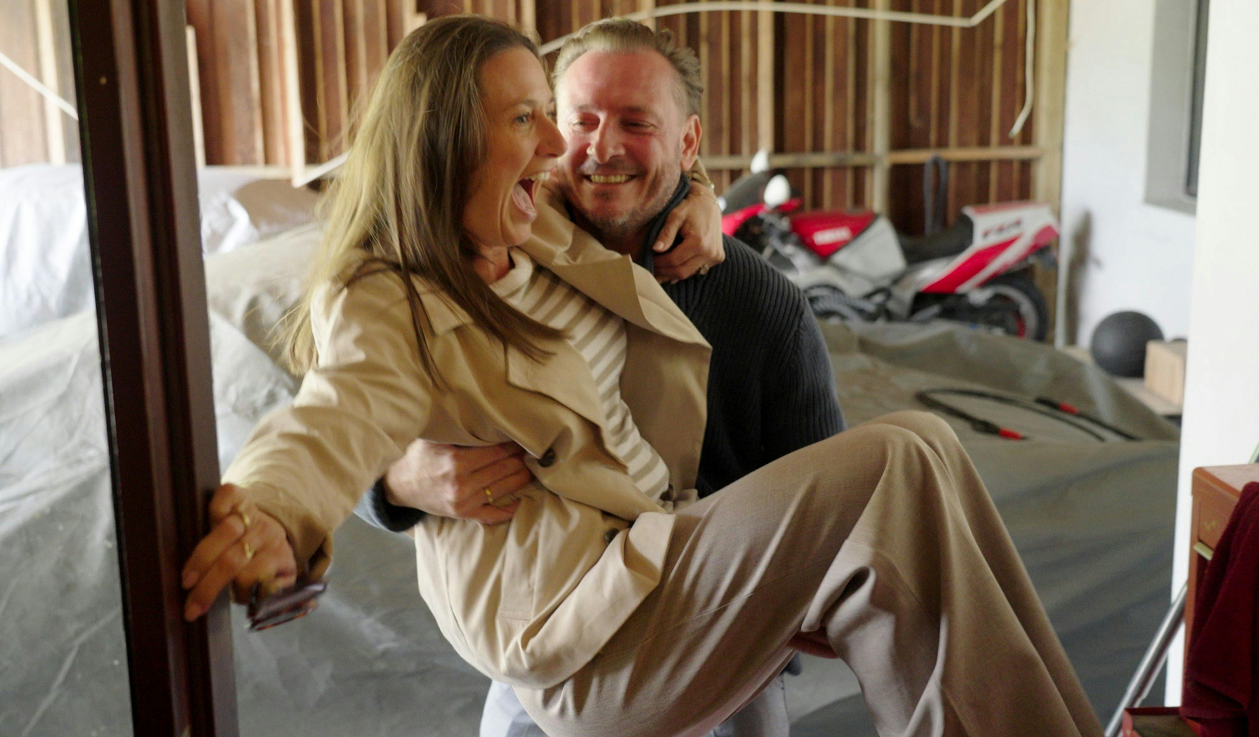 En mand, der bærer en kvinde ind over en dørtærskel fra garage til hus.