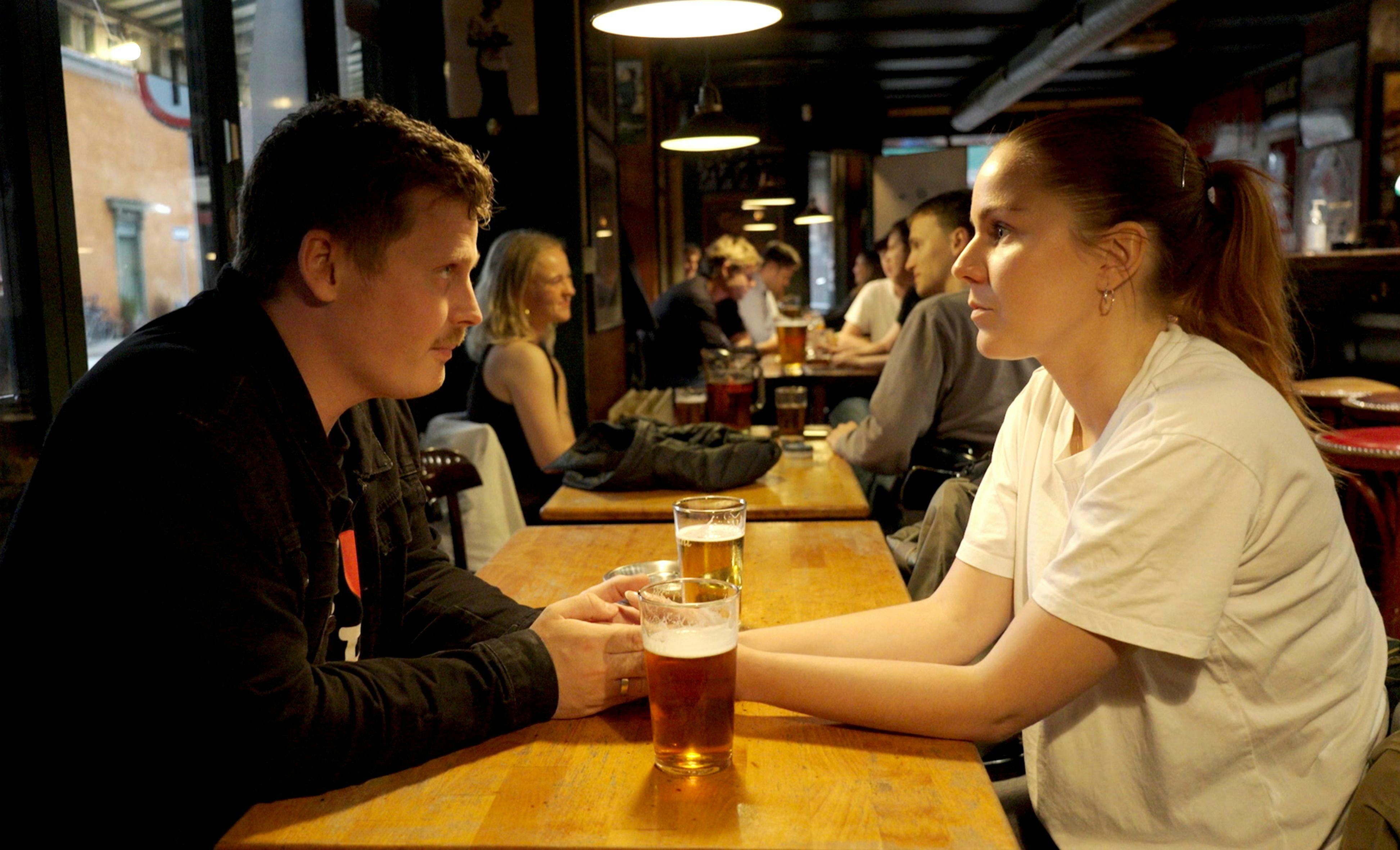 Et ungt par, der sidder over for hinanden på en bar og ser alvorlige ud. Foran dem på bordet står to fadøl.