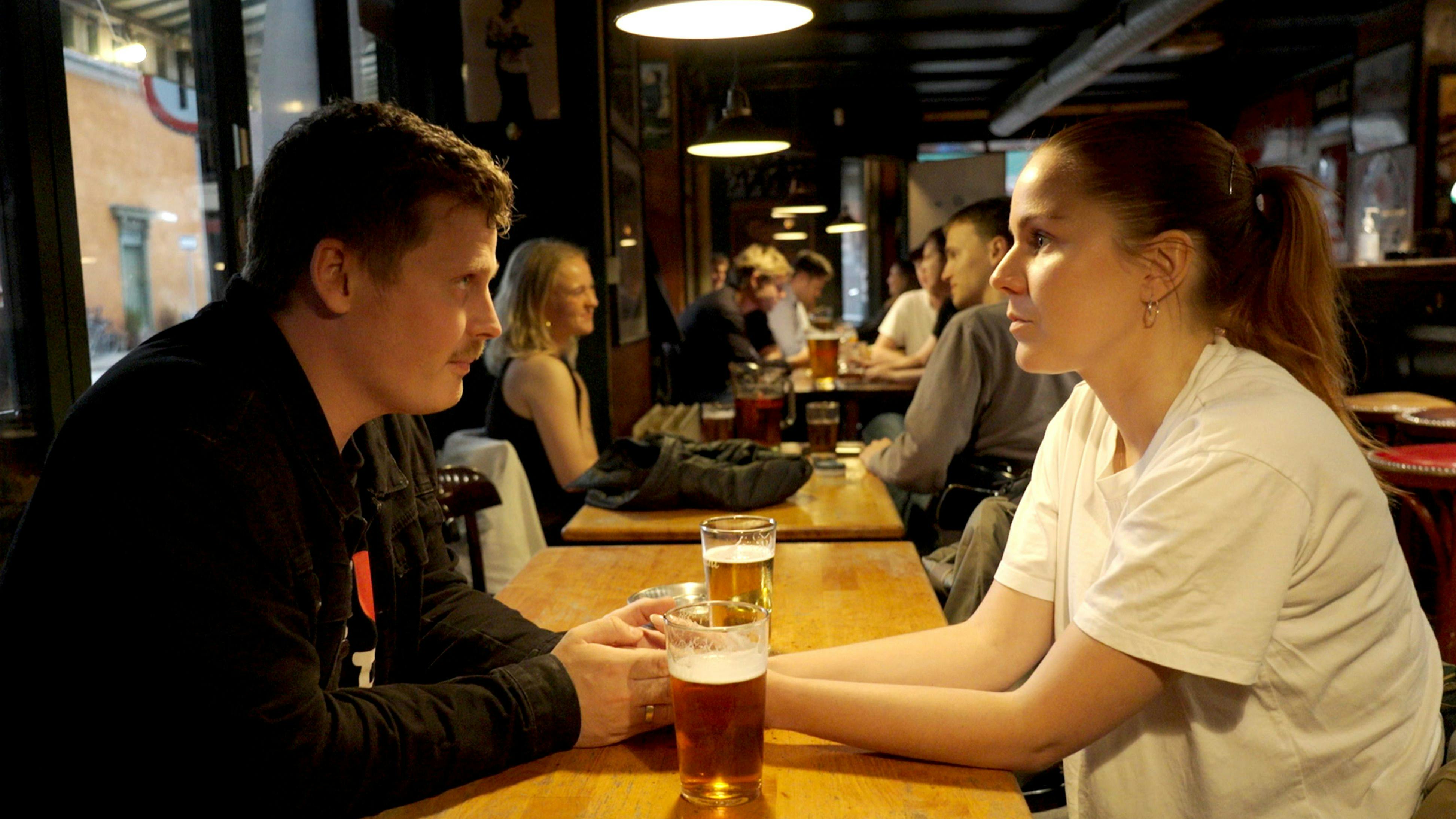 Et ungt par, der sidder over for hinanden på en bar og ser alvorlige ud. Foran dem på bordet står to fadøl.