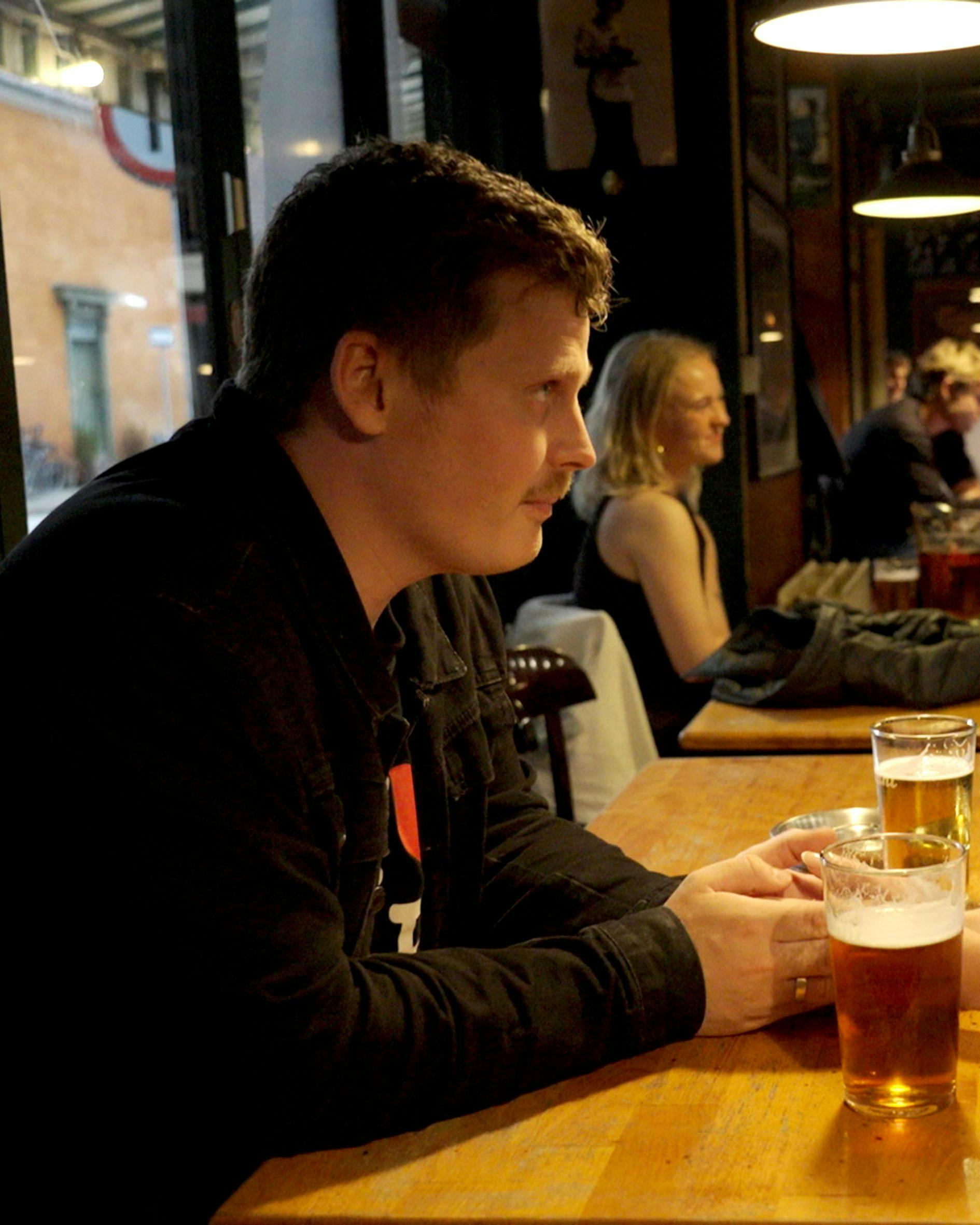 Et ungt par, der sidder over for hinanden på en bar og ser alvorlige ud. Foran dem på bordet står to fadøl.