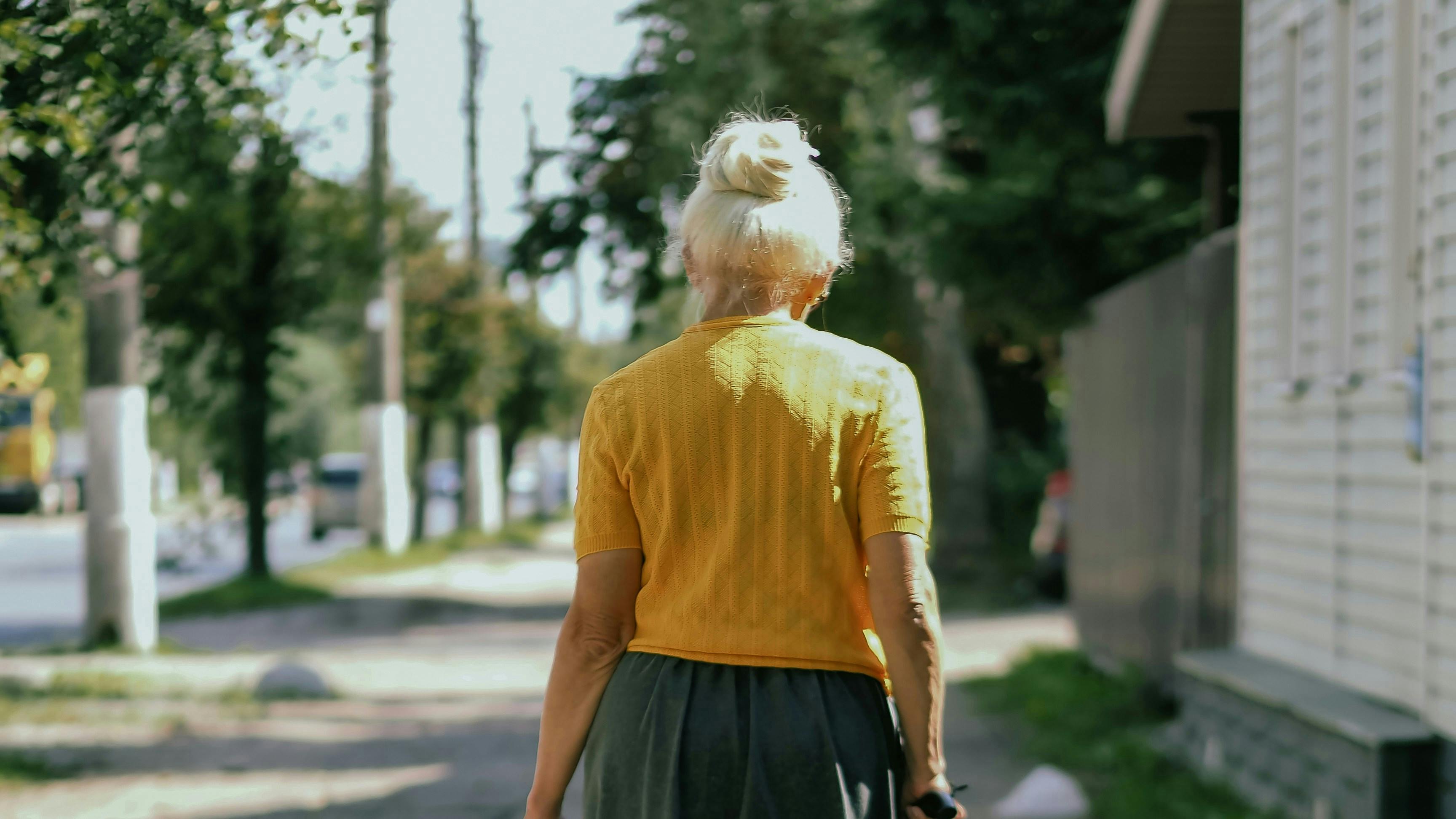 Gammel dame med stok set bagfra på en gade.