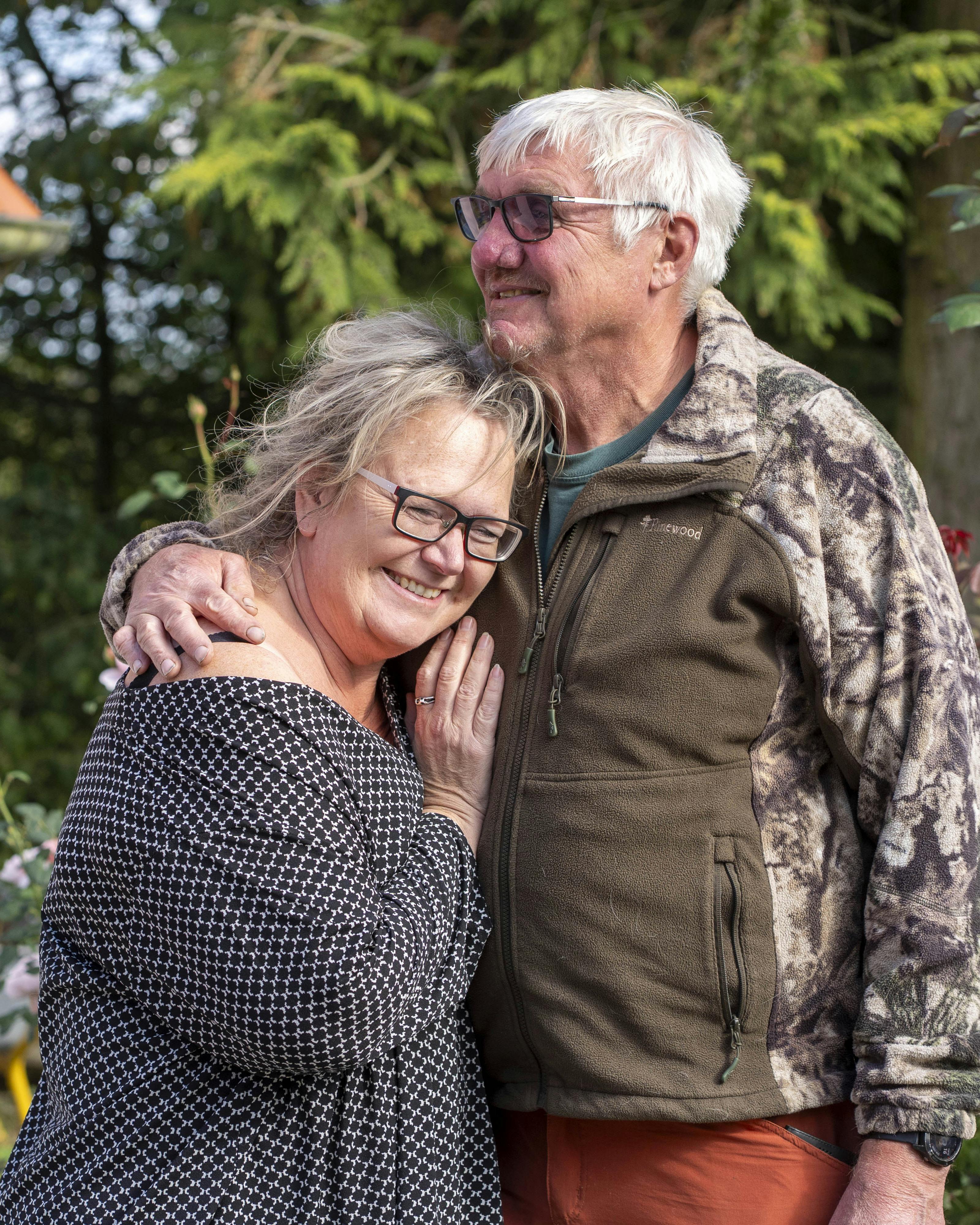 Ældre par krammer foran et hvidt hus med blå vinduer