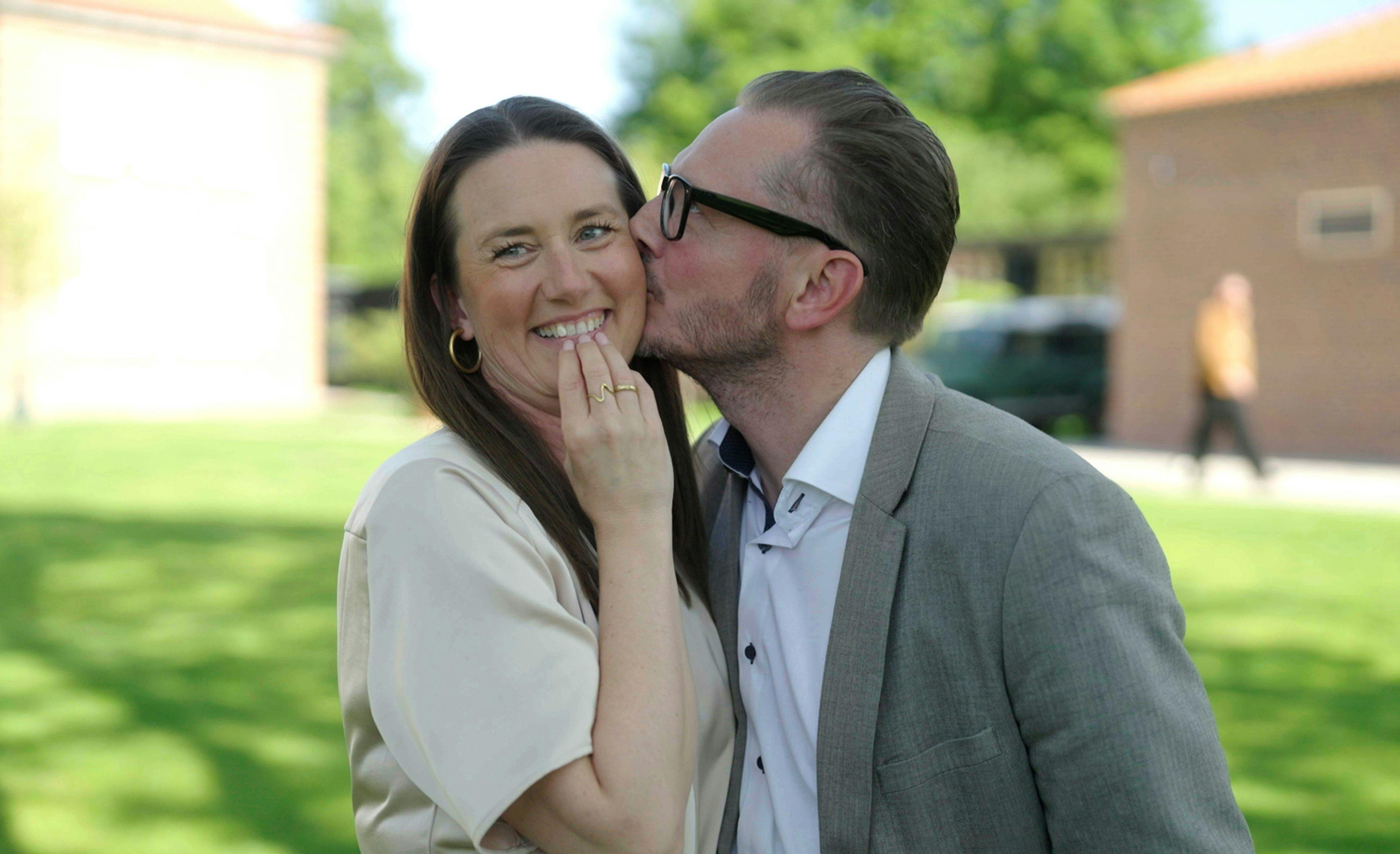 En mand med briller, der kysser en fnisende kvinde på kinden