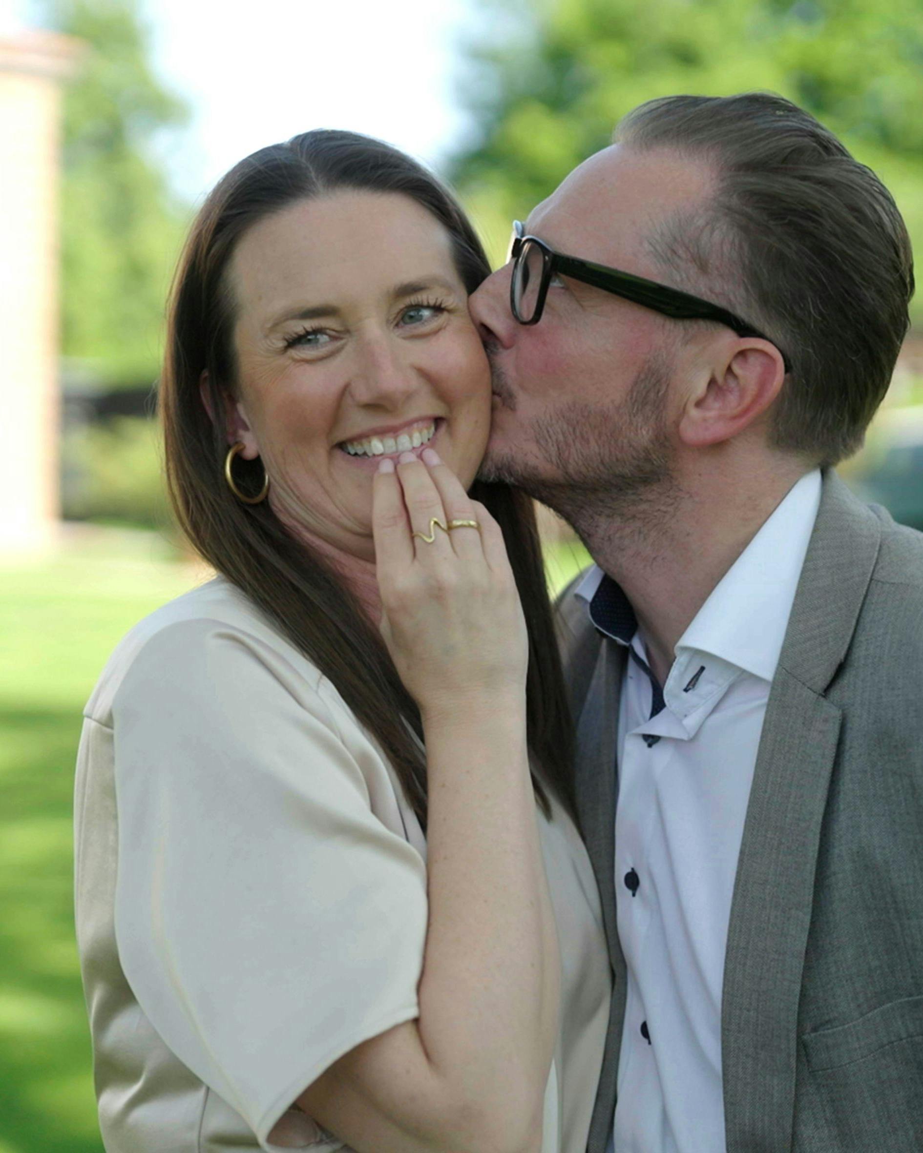 En mand med briller, der kysser en fnisende kvinde på kinden