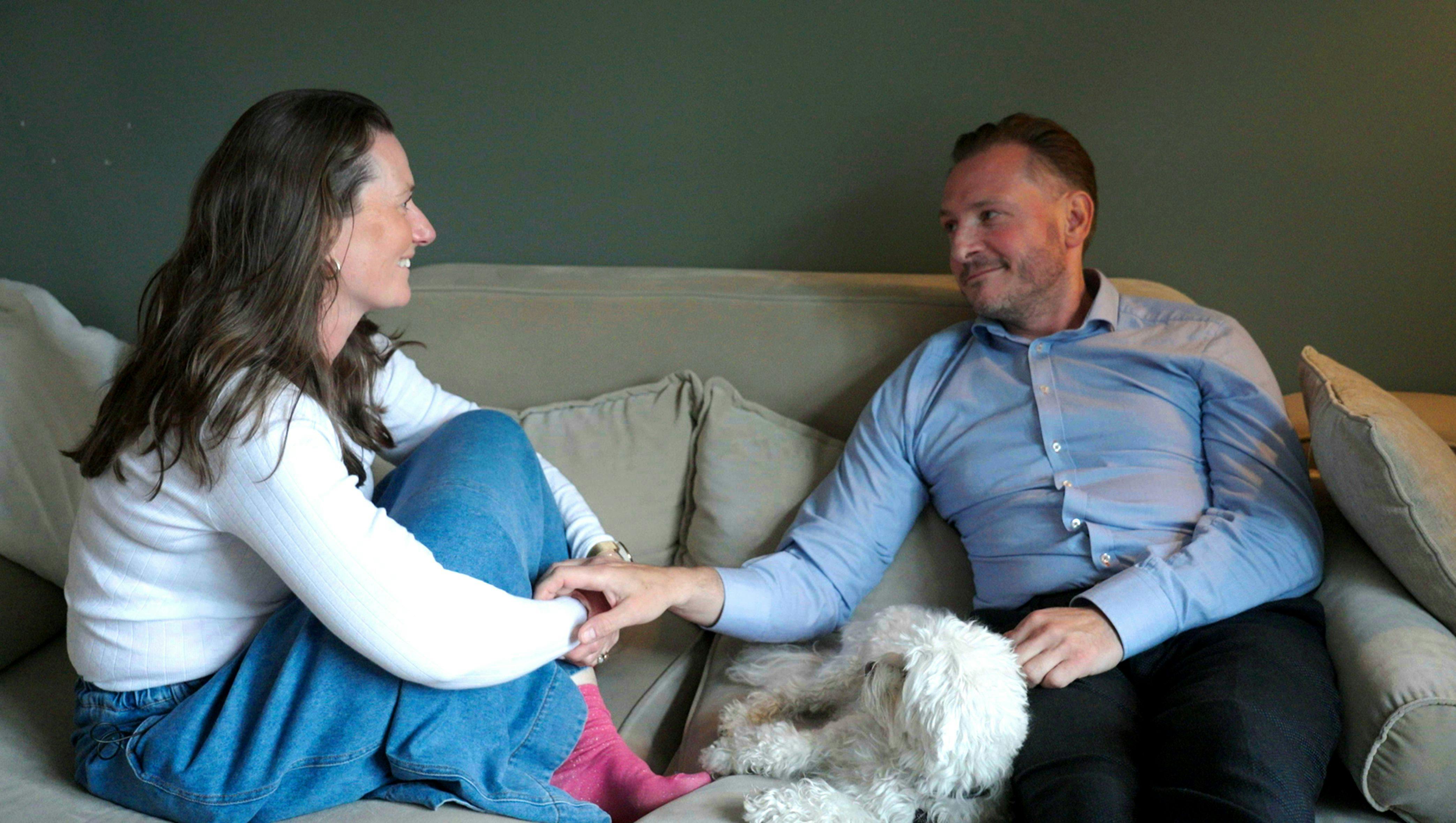 En mand og en kvinde, der sidder i en sofa og holder i hånd. De ser forelskede ud.