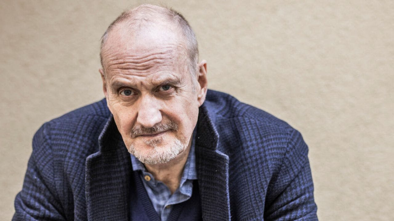 Mand i blåt jakkesæt kigger alvorligt frem foran beige mur