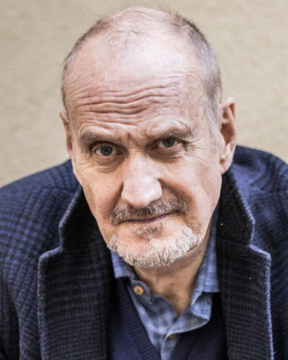 Mand i blåt jakkesæt kigger alvorligt frem foran beige mur