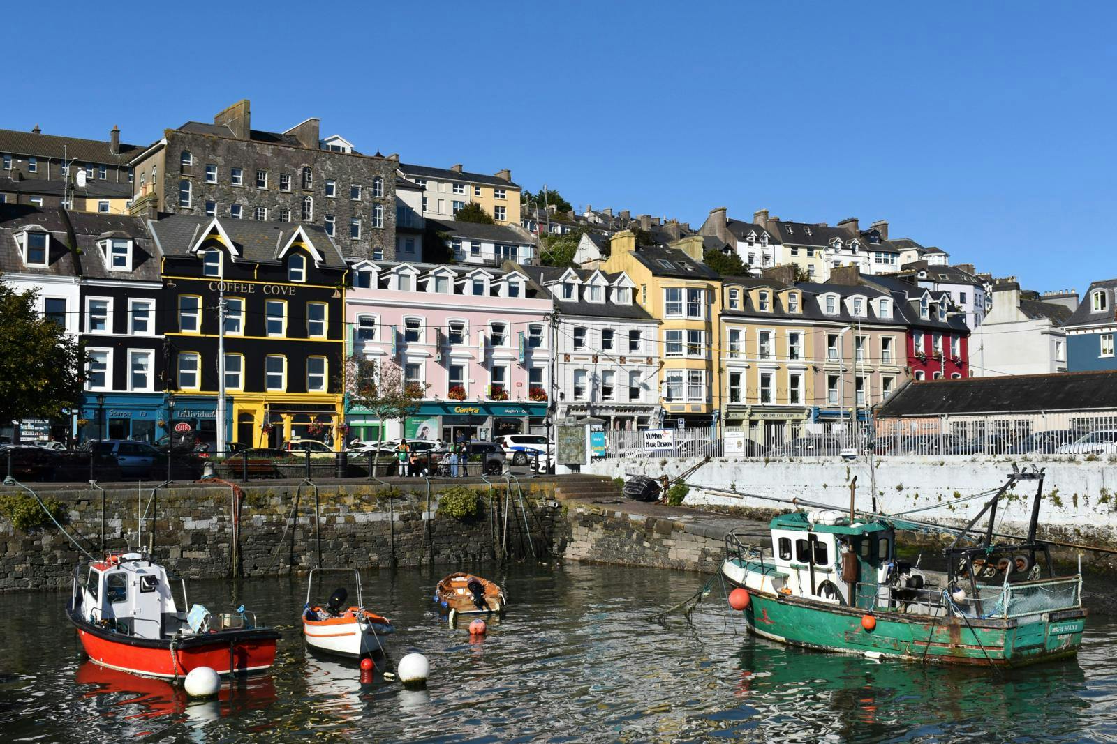 En række gamle huse i forskellige farver foran en lille havn med små både. 