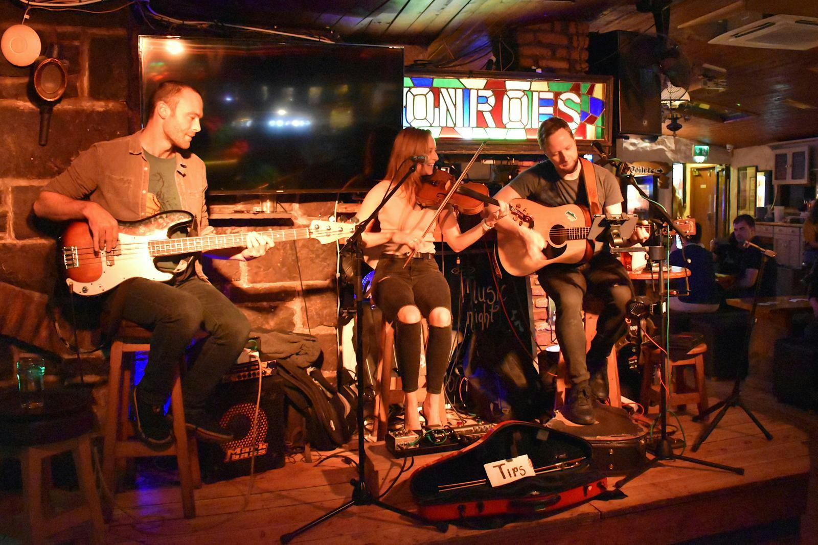 Et lille band på en scene, der spiller guitar, violin og trommer.