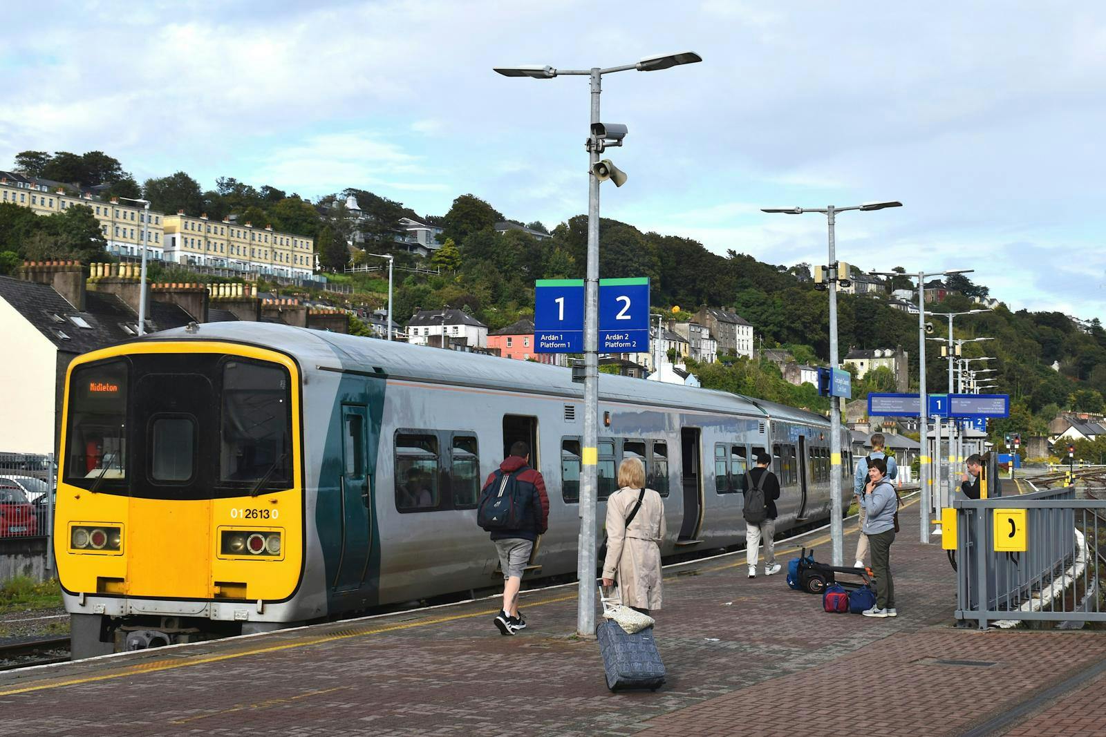 Et gult tog, der holder på en station med nogle få mennesker.