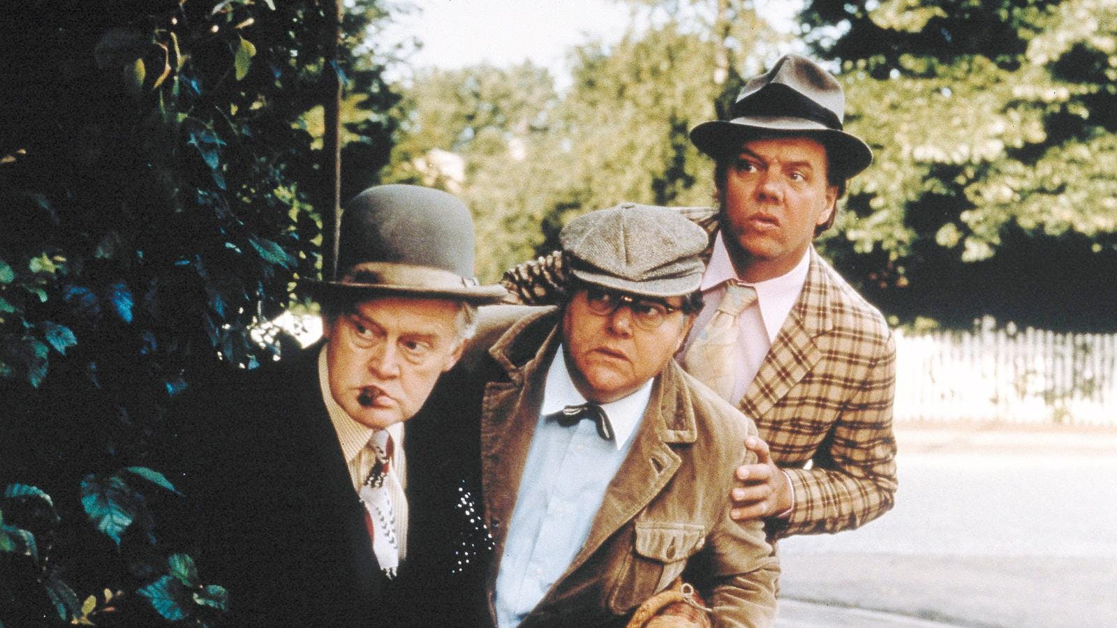 Tre midaldrende mænd - Olsen-banden - der gemmer sig bag et træ og kigger efter noget.