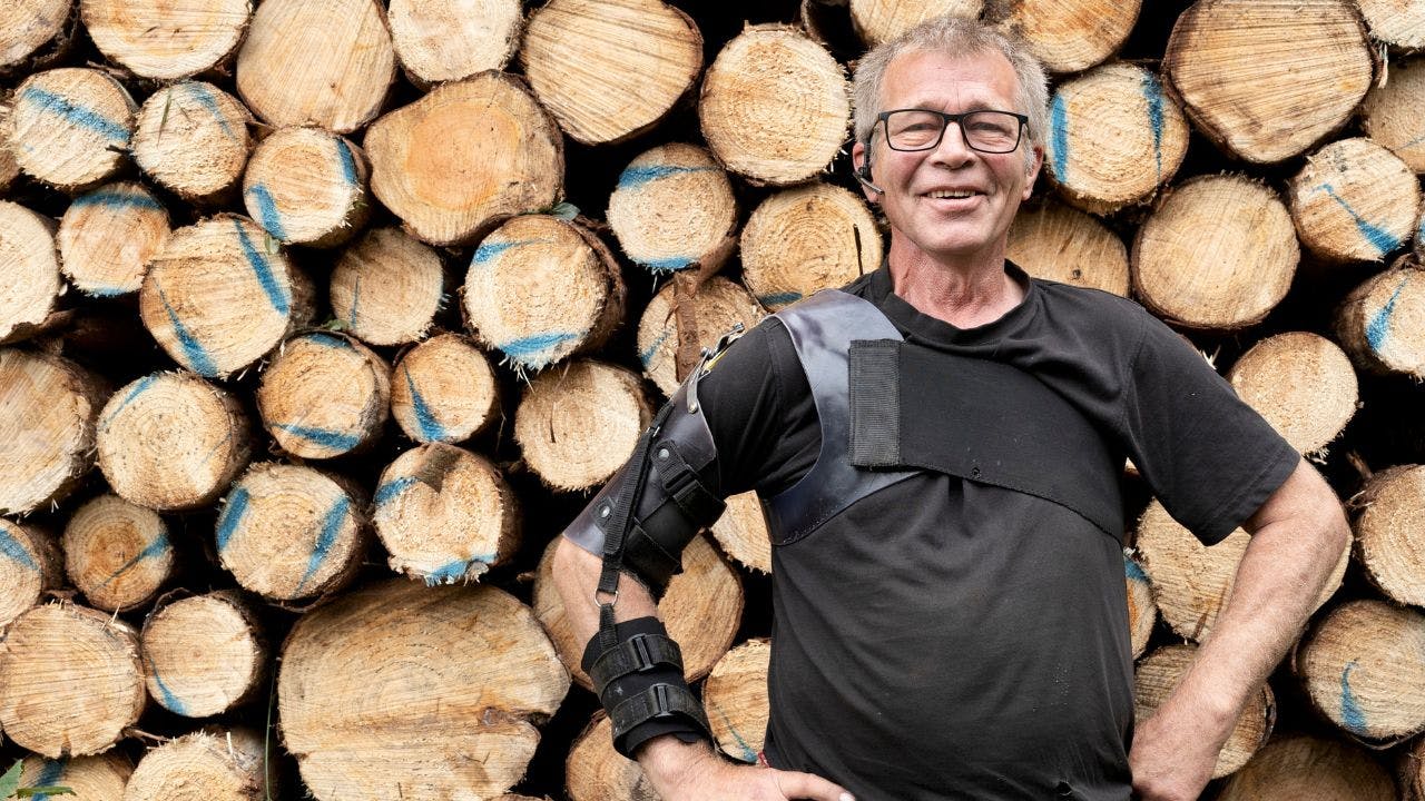 Niels Bach står foran en brændestabel og smiler