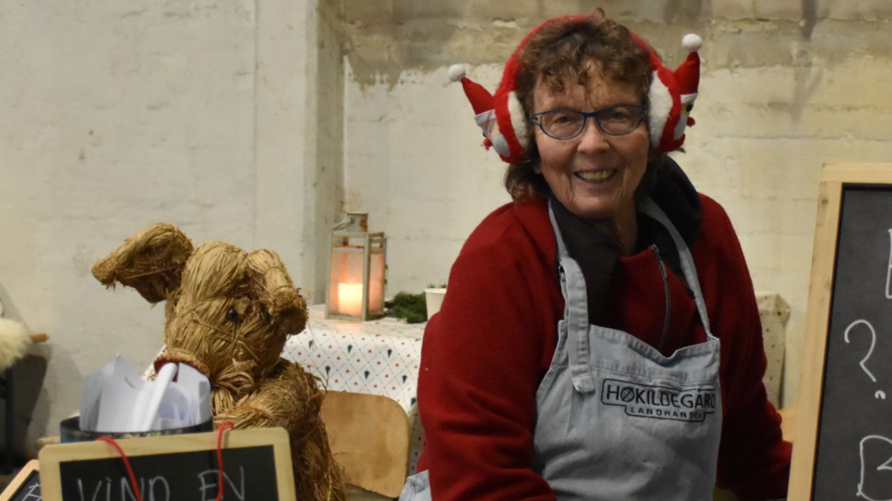 Kvinde står i bod på julemarked og smiler med juleørevarmere på