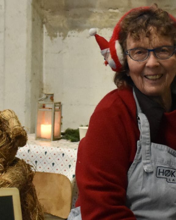 Kvinde står i bod på julemarked og smiler med juleørevarmere på