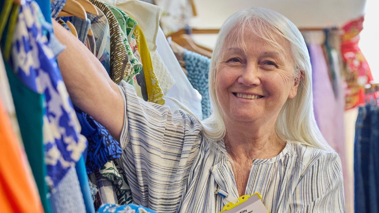 Ældre dame står ved farverigt tøj og arbejder i genbrugsbutik