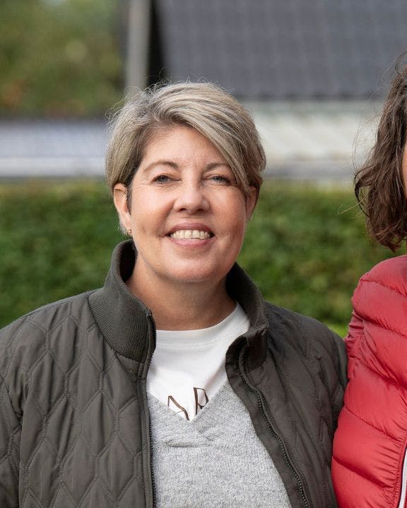 To kvinder står og smiler ved siden af en blomsterbusk