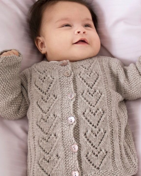 Baby ligger i seng med strikket cardigan på