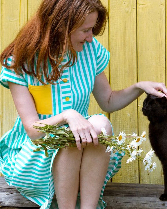 Kvinde sidder foran gulv træhus og aner en sort kat