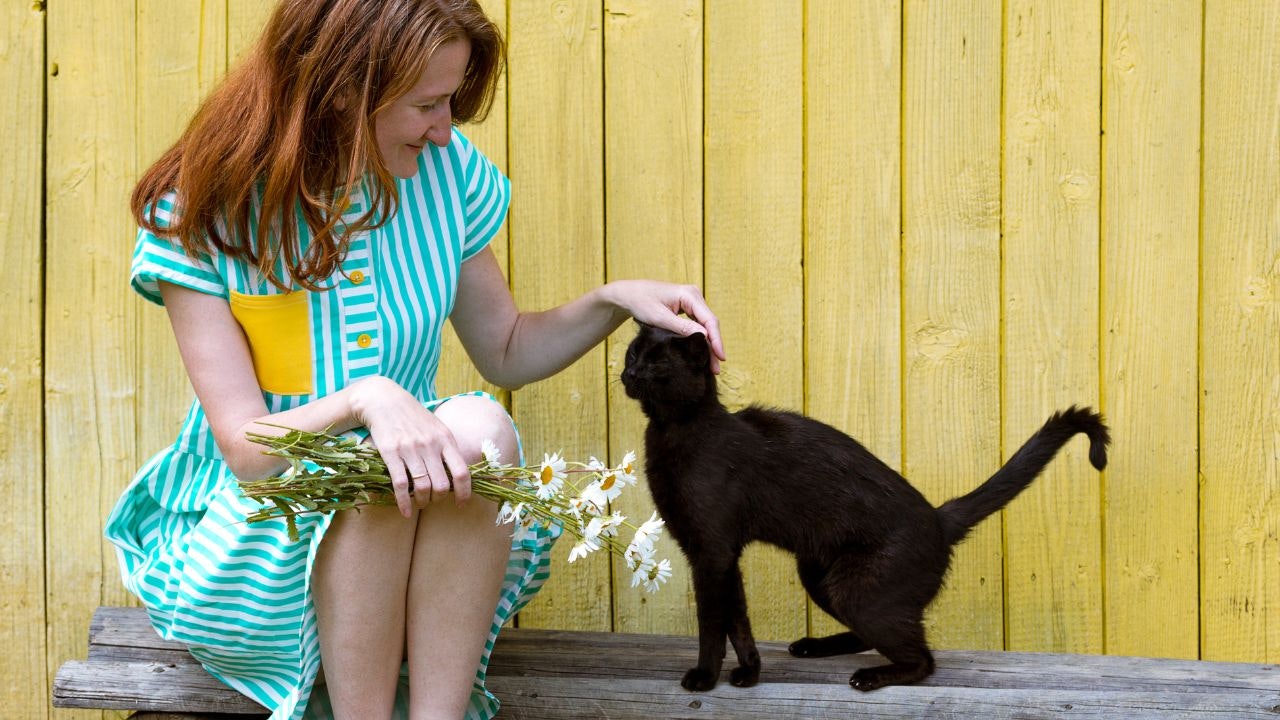 Kvinde sidder foran gulv træhus og aner en sort kat