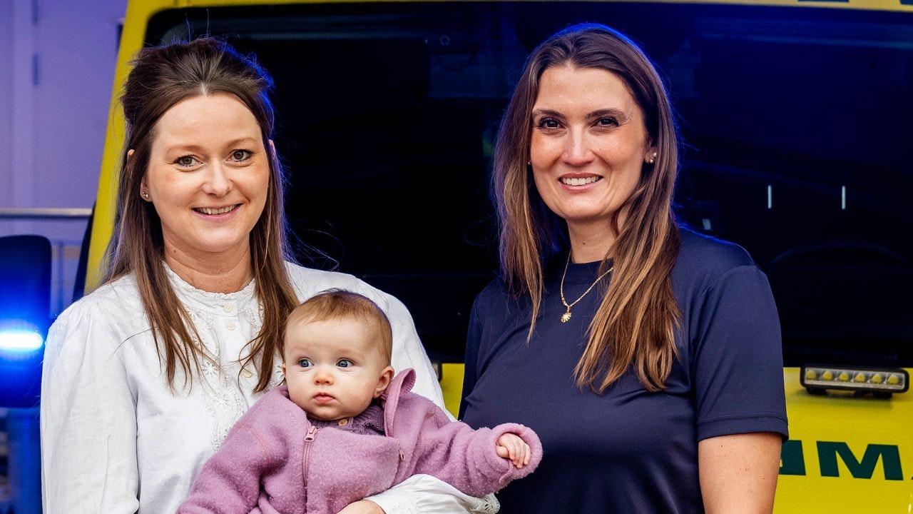 To kvinder står foran en ambulance, og den ene har en baby i armene
