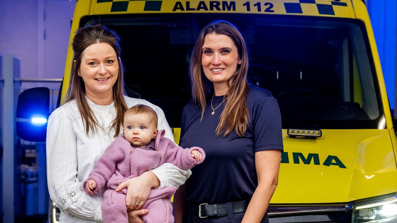 To kvinder står foran en ambulance, og den ene har en baby i armene