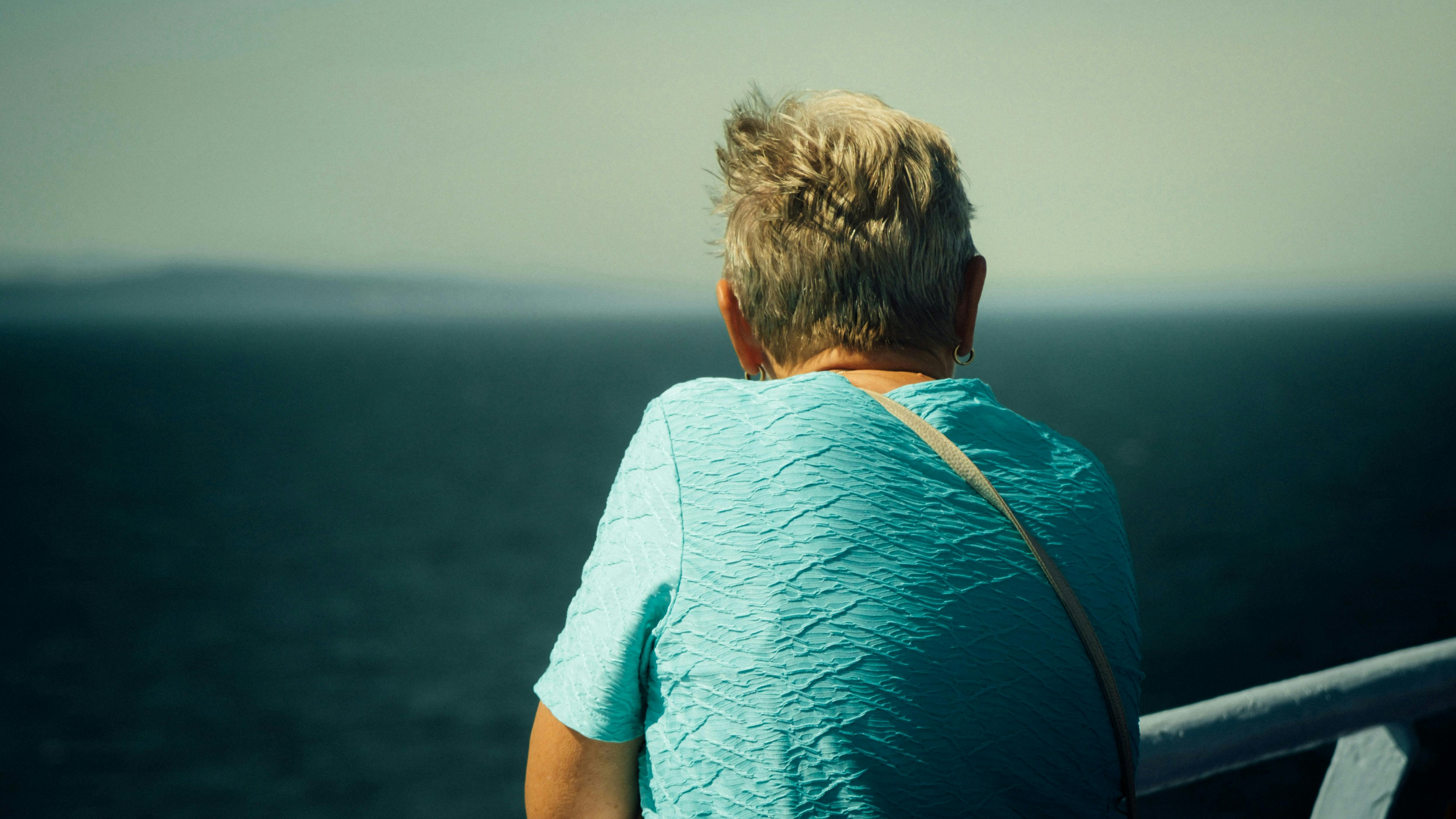 Kvinde set bagfra, der står ved en ræling og kigger ud over havet.
