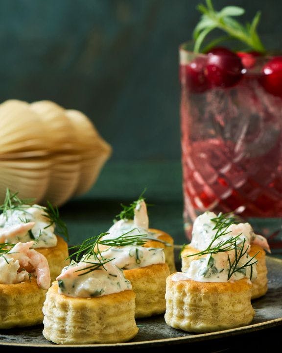 Rød Gin & Tonics med tranebær står ved siden af krustader med rejesalat på et fad