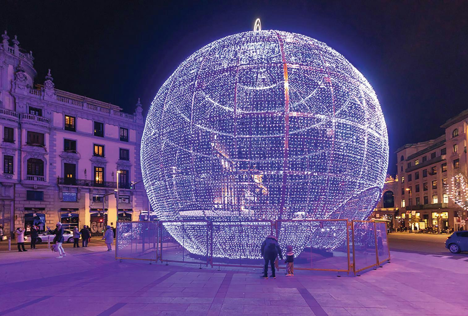En stor lyslilla glaskugle på en plads badet i lilla lys.
