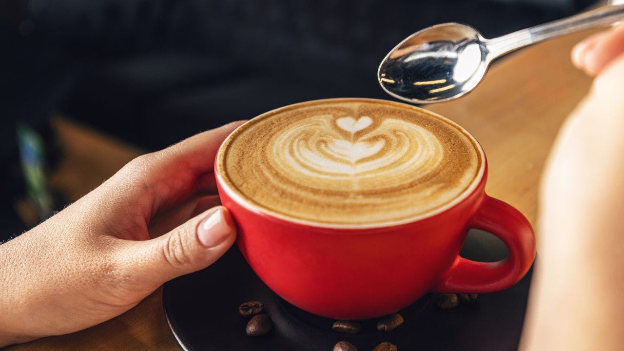 Kvindehånd holder om en kop kaffe med mælkeskum formet som et hjerte