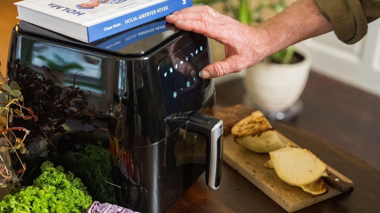 Mandehånd tænder for en airfryer, der står på en køkkenbord