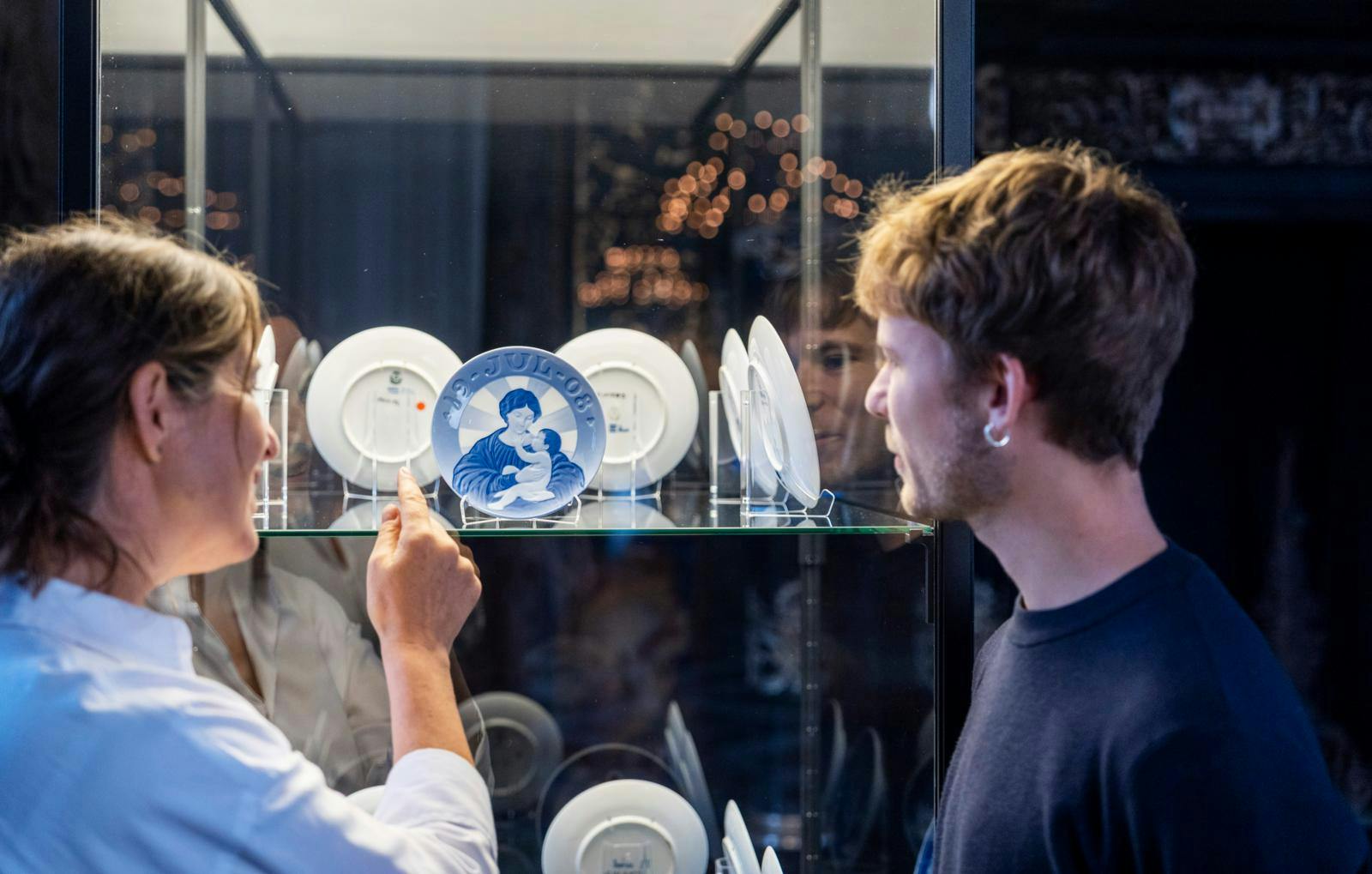 En kvinde, der peger på en juleplatte i en glasmontre. Ved siden af står en mand, der også kigger på platten. 