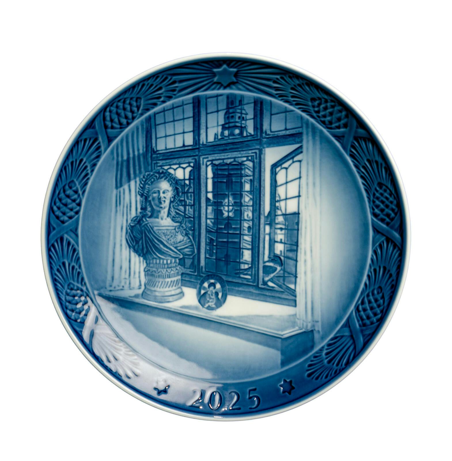 En juleplatte med motiv af et vindue med udsigt til et kirketårn og en buste. i vindueskarmen.