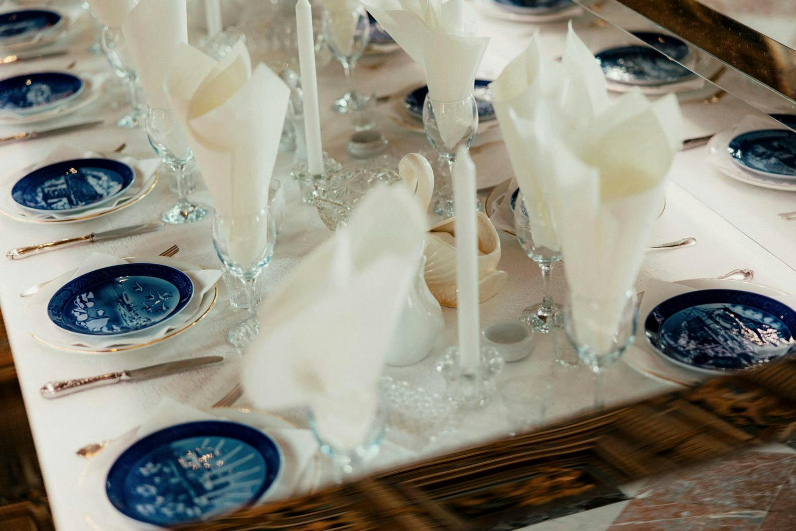 Et langbord dækket med stofservietter, glas, bestik og juleplatter.