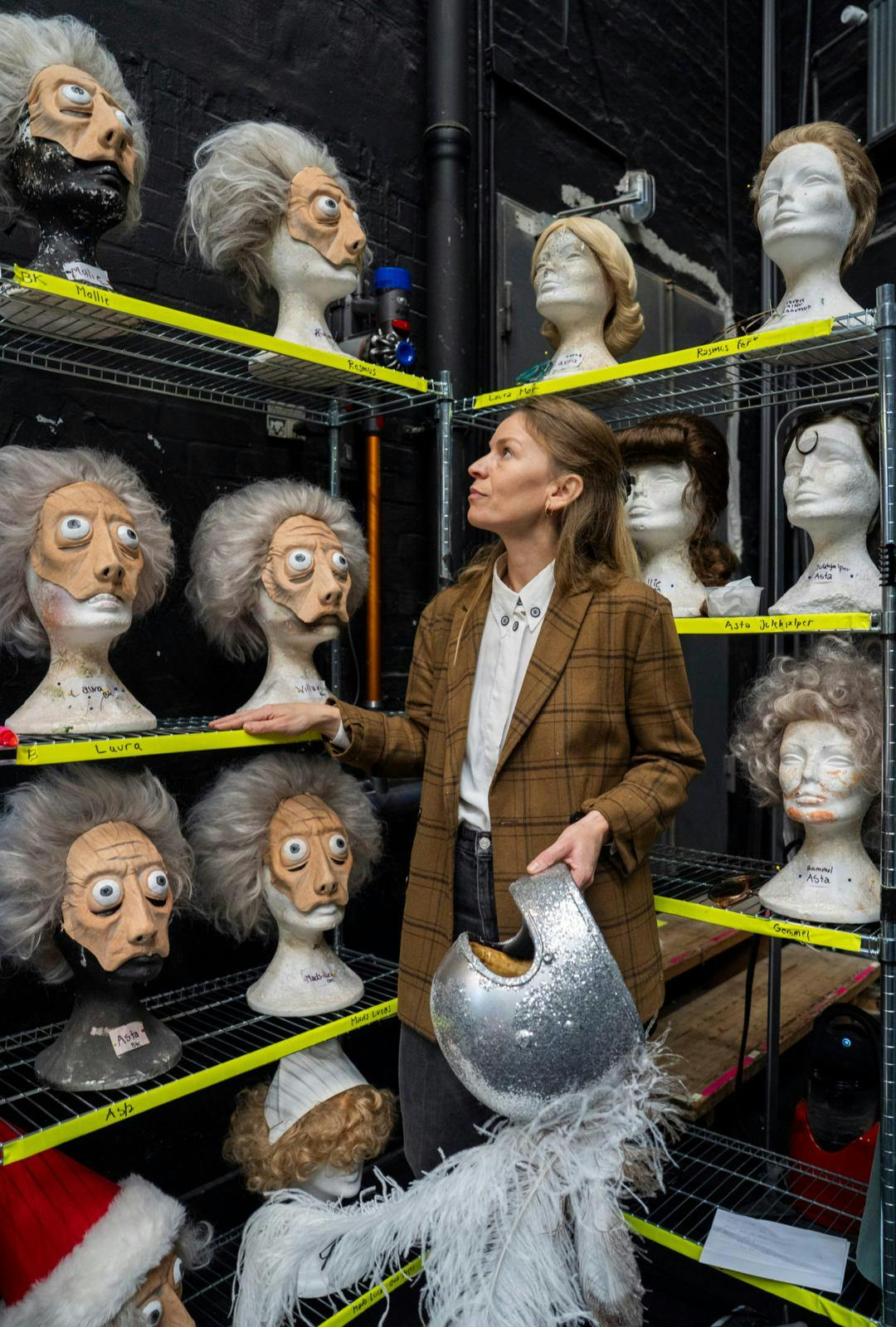 En kvinde, der kigger på en masse masker og har en ridderhjelm i hånden.