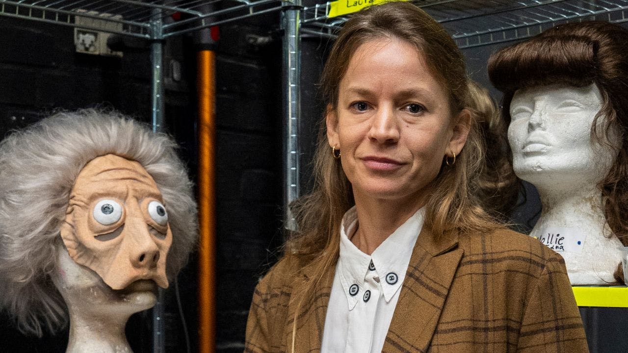 Kvinde står i ved hylder, hvor der ligger en maske og en paryk