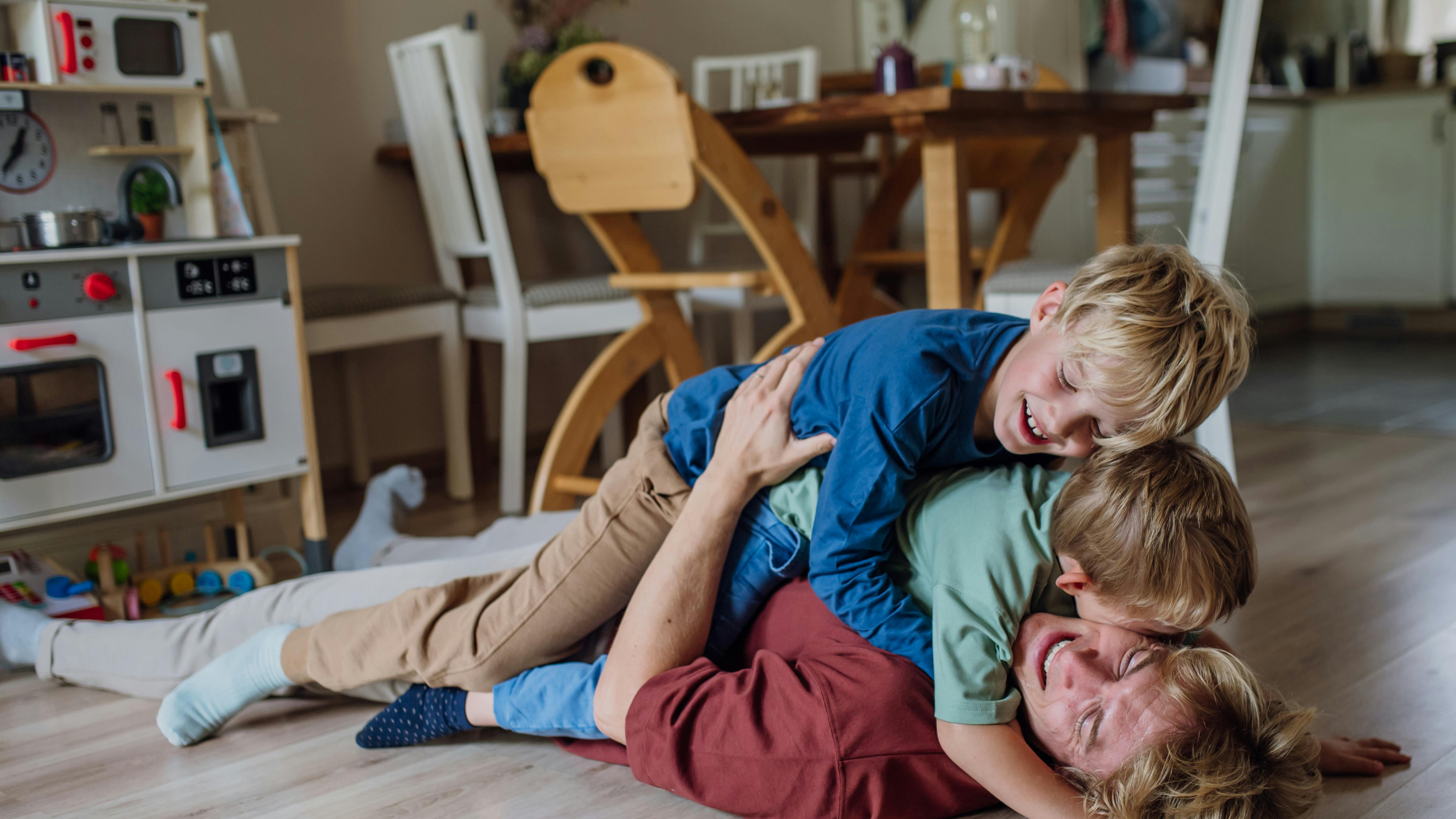 En far ligger på gulvet med sine to sønner ovenpå sig