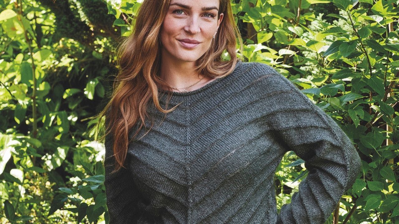 Kvinde med strikket sweater foran grønne blade