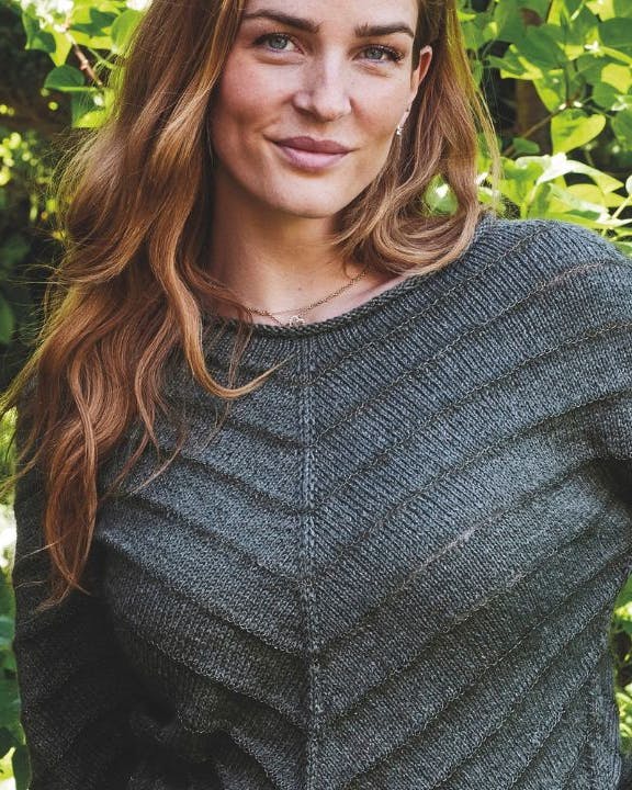 Kvinde med strikket sweater foran grønne blade