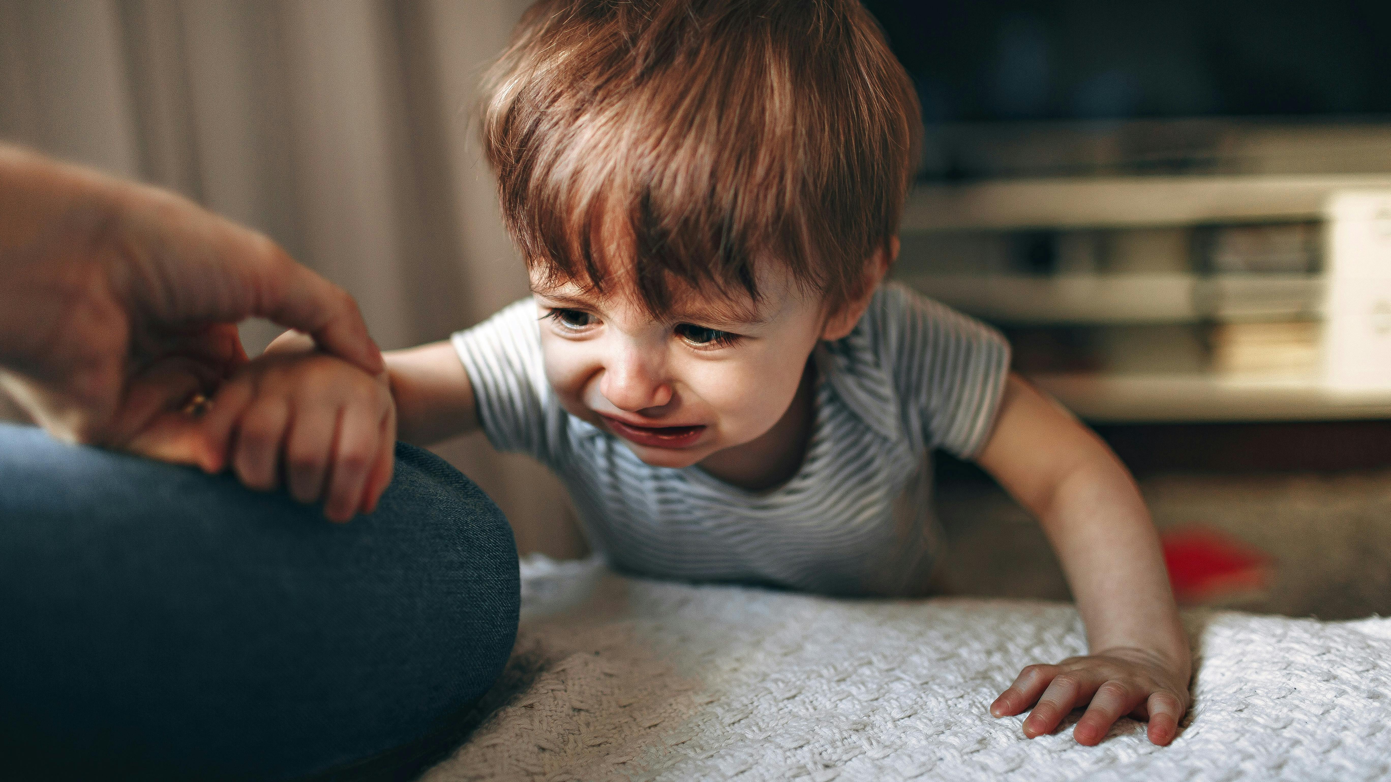 Et lille barn, der ser ked ud af det, mens han forsøger at kravle op til en udstrækt hånd.