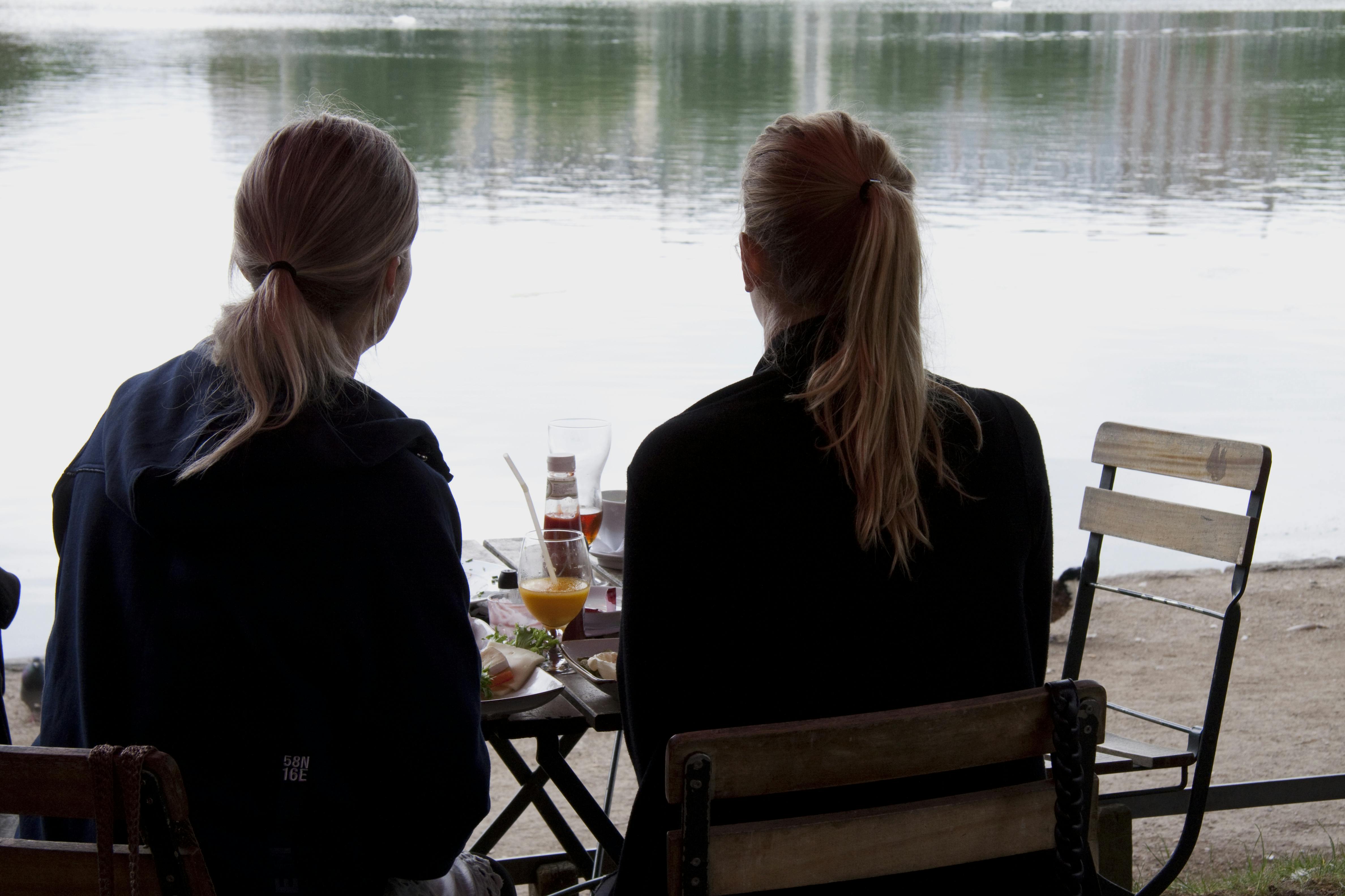 To kvinder med ryggen til spiser morgenmad ved vandet