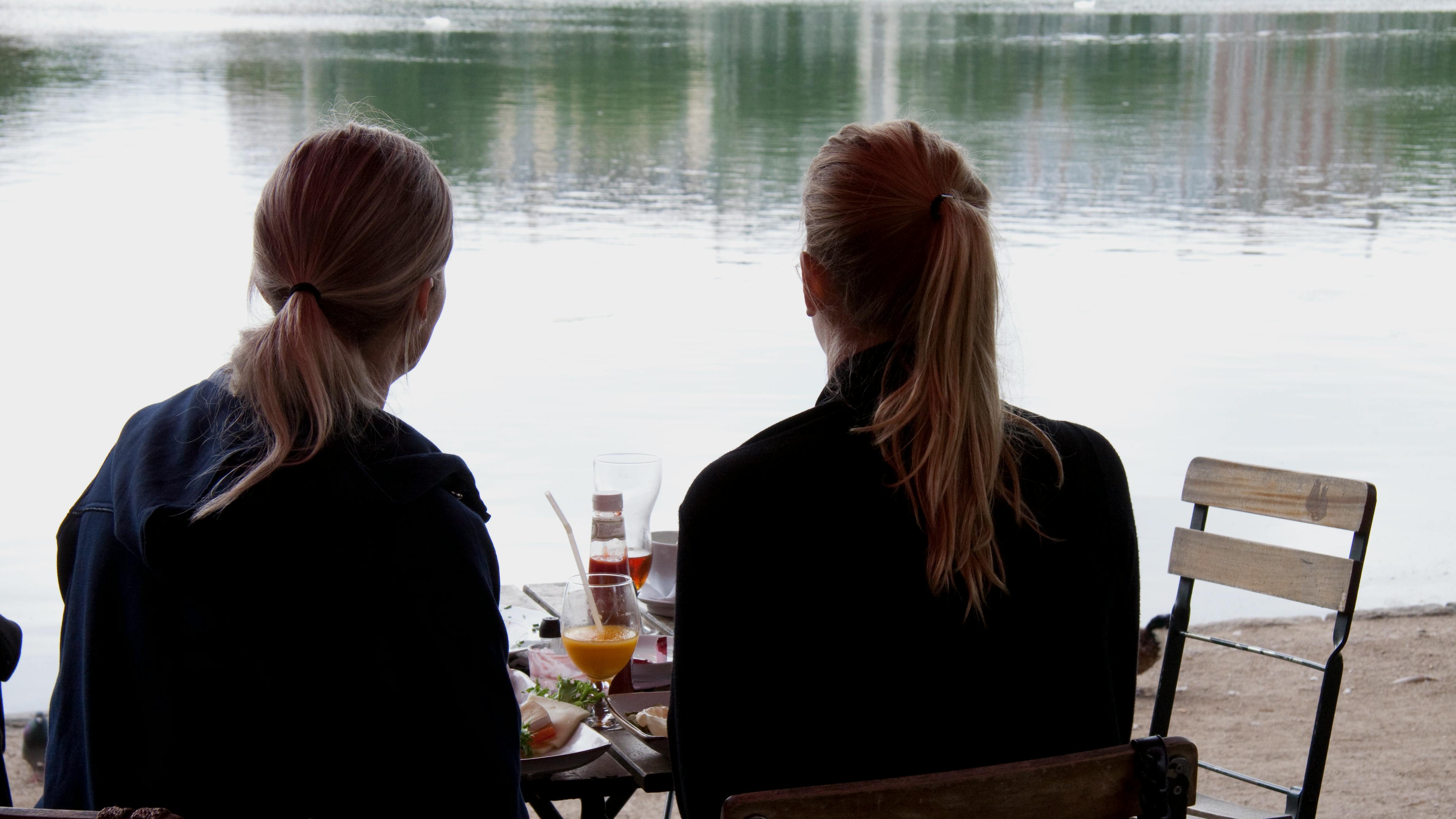To kvinder med ryggen til spiser morgenmad ved vandet