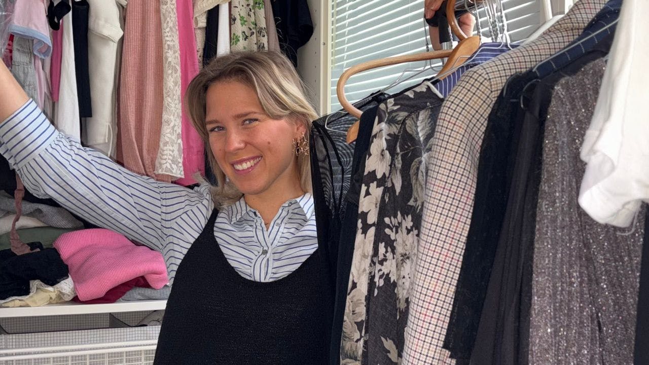 Skribenten står foran tøjskab ved siden af tøjstativ med masser af genbrugstøj