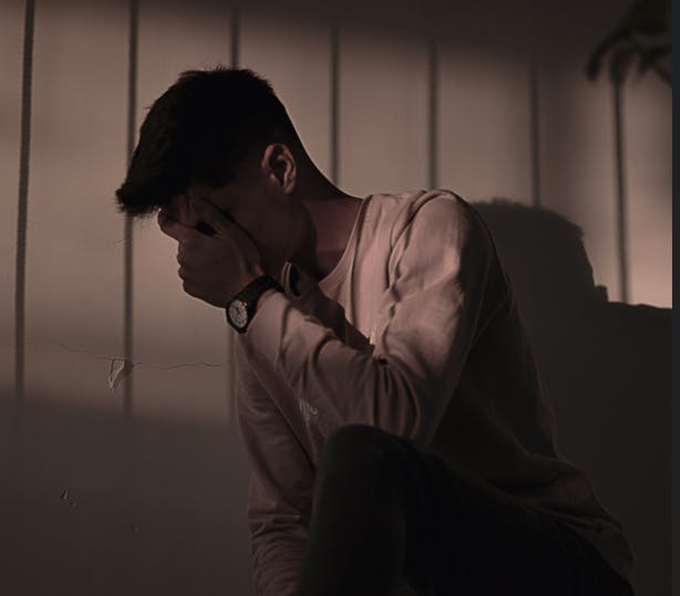 En dreng, der sidder i mørke og gemmer ansigtet i hænderne 