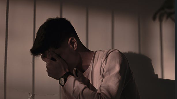 En dreng, der sidder i mørke og gemmer ansigtet i hænderne