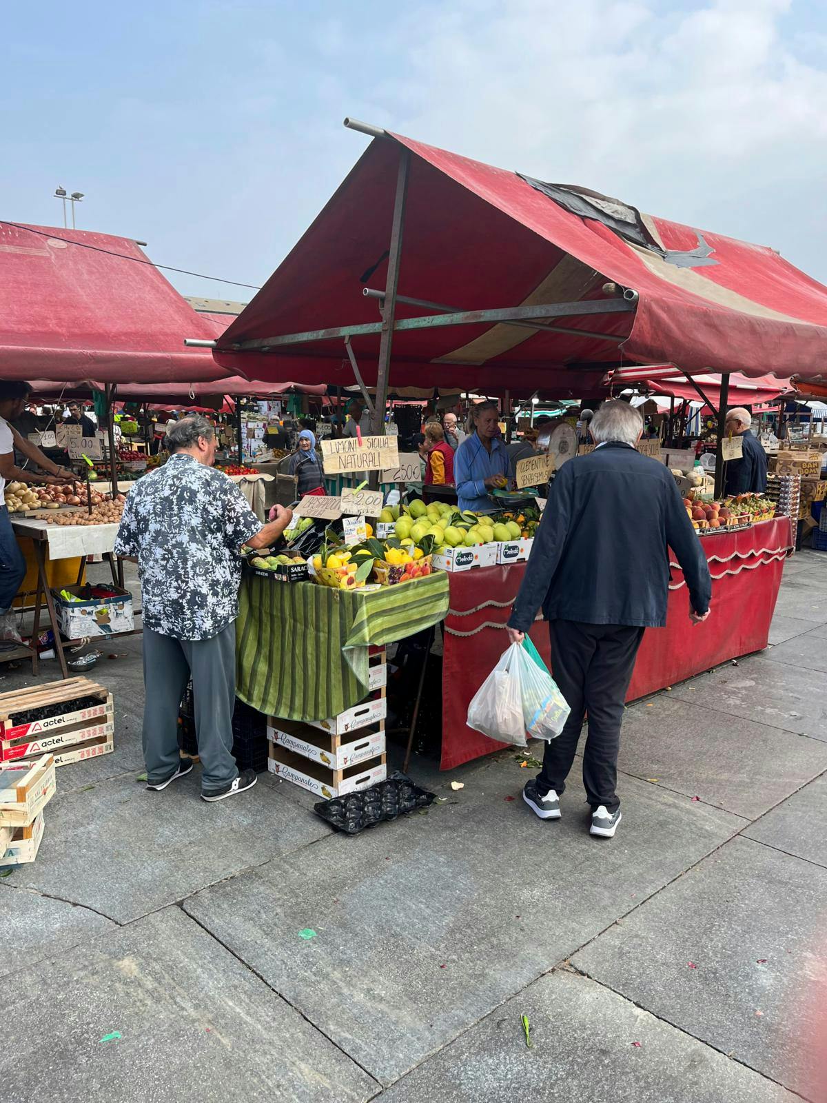 Markedsboder med grøntsager og to handlende foran.