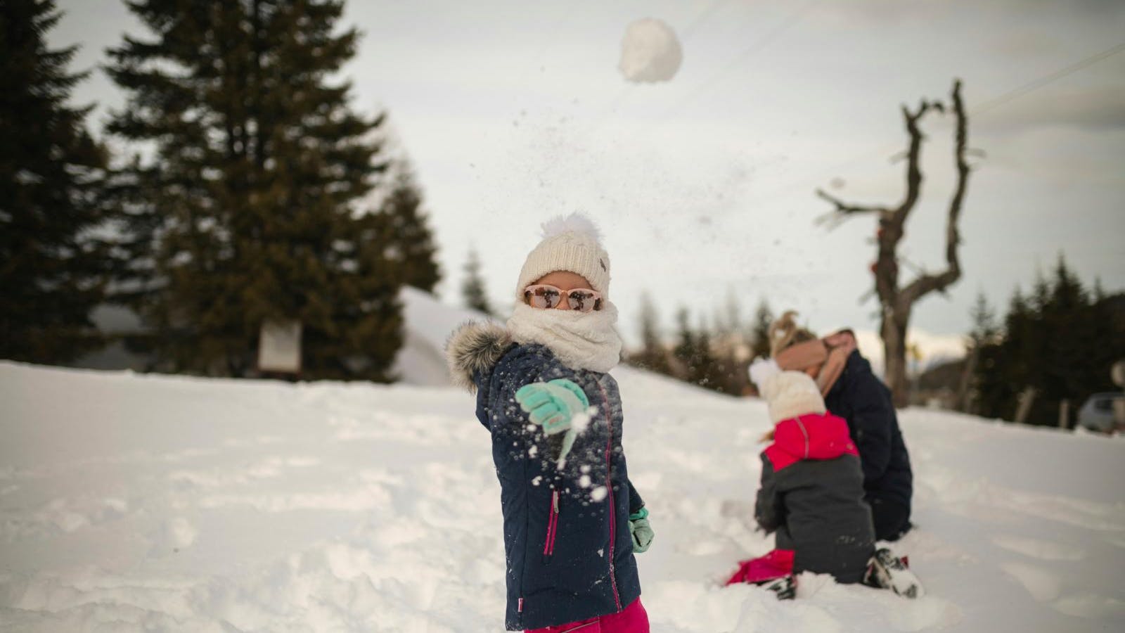 Et barn i vintertøj, der kaster en snebold mod kameraet